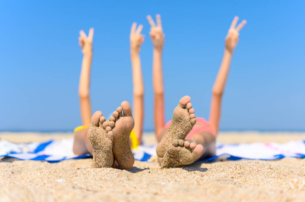Концепція чудового морського відпочинку. Дитячі ноги з приклеєним піском на тлі моря і піднятими руками. Вибірковий фокус і мала глибина різкості
. - Фото, зображення