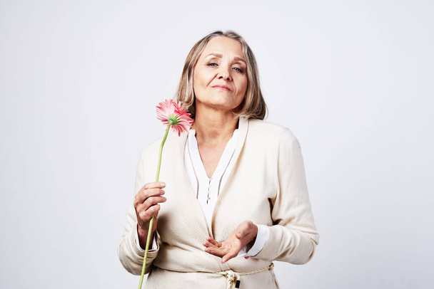 elderly woman in a robe holding a flower gift light background - Φωτογραφία, εικόνα