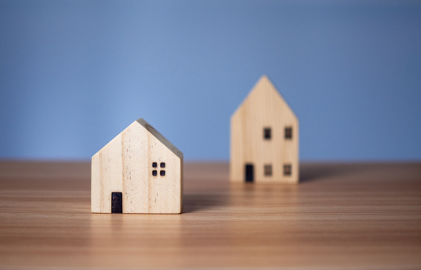 Два деревянных дома модели, расположенных на деревянном столе. на светло-синем фоне - Фото, изображение