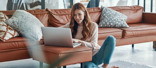 Beautiful young woman using laptop and smiling while spending time at home - Φωτογραφία, εικόνα
