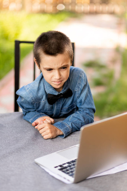 Il ragazzo scolaro allegro è impegnato in lezioni attraverso un computer portatile a casa in giardino. Lezioni online per bambini - Foto, immagini