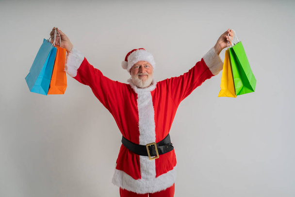 cheveux gris barbu santa claus aller faire du shopping tenir x-Noël sacs de Noël sur un fond blanc, tenant sac cadeau de Noël - Photo, image