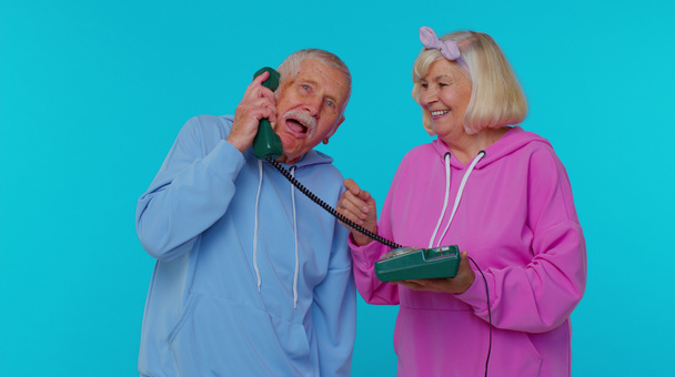Сумасшедшая бабушка дедушки разговаривает по винтажному телефону, дурачится, строит глупые рожи - Фото, изображение
