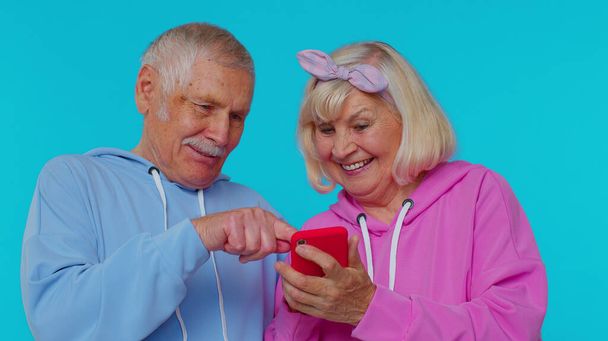 高齢の祖父母の年金受給者は、携帯電話を使って新しいポスト、ブラウジング、オンラインショッピングを入力します。 - 写真・画像