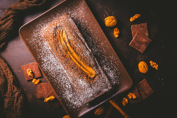 Домашний веганский банановый хлеб или торт с орехами, шоколадом и корицей на коричневом фоне - Фото, изображение