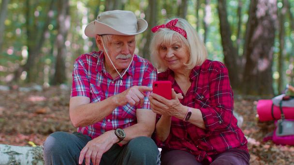 Vieil homme séduisant femme routard planification itinéraire de voyage en forêt sur téléphone portable en bois - Photo, image