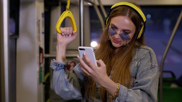 Young girl using mobile phone internet social network listening music traveling by public city bus - Фото, зображення