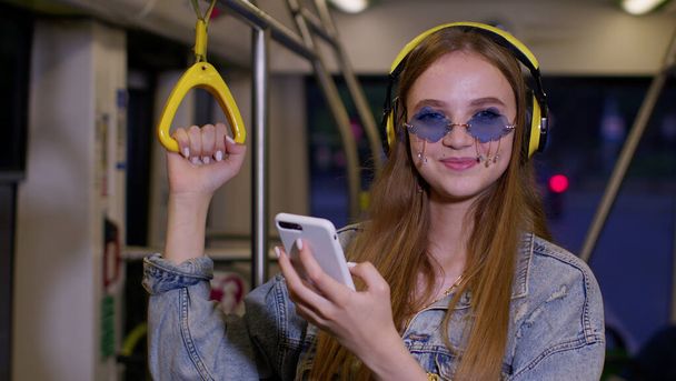 Young woman wearing headphones listening music, funny relax dancing while traveling by bus to city - Foto, afbeelding