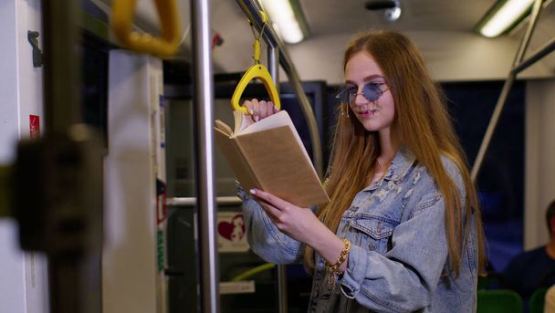 Portret van aantrekkelijke jonge volwassen vrouw verblijf in lege metro trein en het lezen van interessante boek - Foto, afbeelding