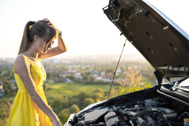 Junge Autofahrerin steht neben ihrem Auto mit offener Motorhaube und hat Motorproblem. - Foto, Bild