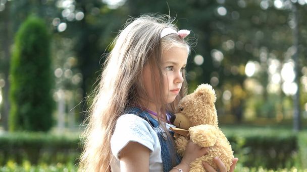 Pretty child girl playing with her favorite teddy bear toy outdoors in summer park. - Foto, afbeelding
