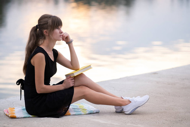 Γυναίκα φοιτήτρια κάθεται στο καλοκαιρινό πάρκο διαβάζοντας βιβλίο σε εξωτερικούς χώρους. Εκπαίδευση και κατάρτιση. - Φωτογραφία, εικόνα