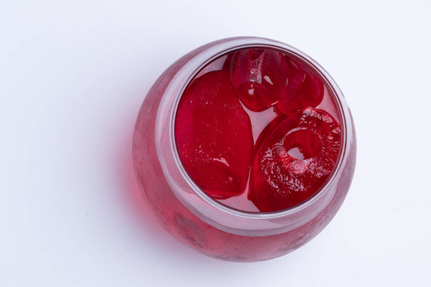 Agua roja con hielo en un vaso transparente sobre un fondo blanco. - Foto, Imagen