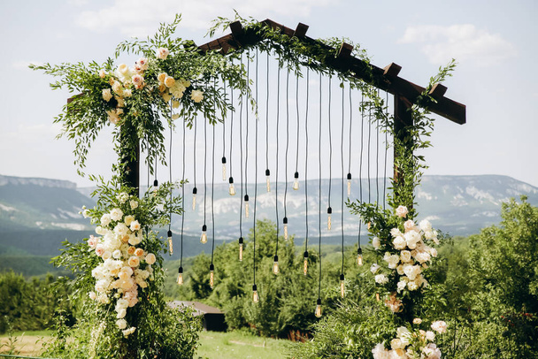 Łuk weselny w stylu rustykalnym z białymi kwiatami w parku z żarówkami. - Zdjęcie, obraz
