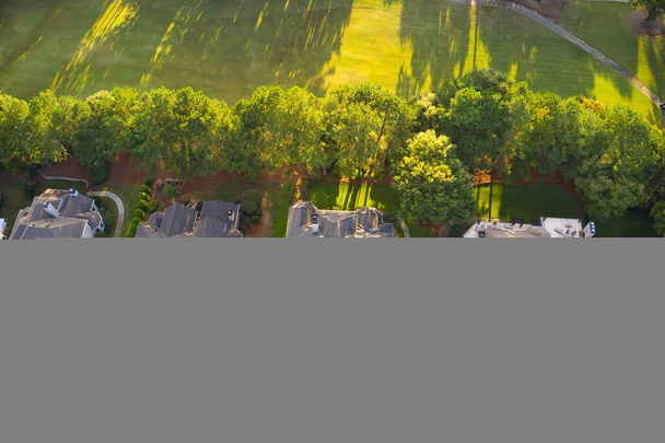 Вид с воздуха на красивые дома, крыши и пышные зеленые ландшафтные дворы в высококлассном подразделении в пригородах США, снятый в течение Золотого часа ранней весной. - Фото, изображение