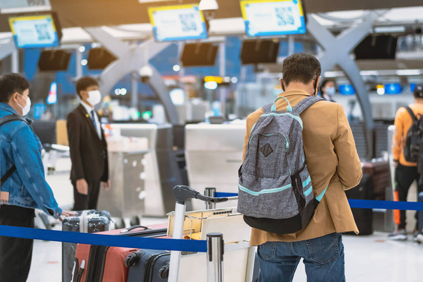 Rückansicht von Flugpassagieren, die eine Gesichtsmaske tragen, um Coronavirus (Covid-19) zu verhindern, warten am Check-in-Schalter im Flughafen, während das Personal eine Gesichtsmaske trägt. Neues normales Reisekonzept nach Covid-19-Pandemie. - Foto, Bild