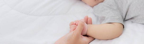Молодая мама трогает за руку маленькую девочку с лаской на кровати в спальне, мама любит новорожденного и заботится о нем, женщина с выражением лица вместе с ребенком, родитель и дочь, понятие семьи. - Фото, изображение