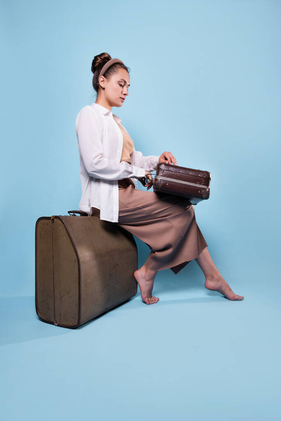 cute young woman in summer pants and a white shirt is sitting on suitcases - Foto, Imagem