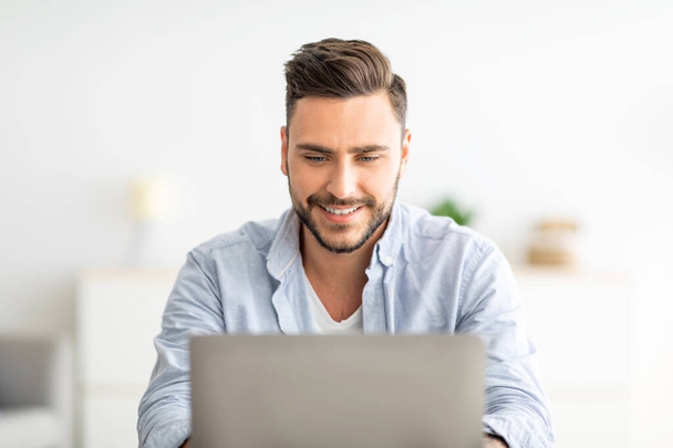 Home office concept. Closeup portrait of happy guy working on pc laptop, sitting at workplace at home interior - Фото, изображение
