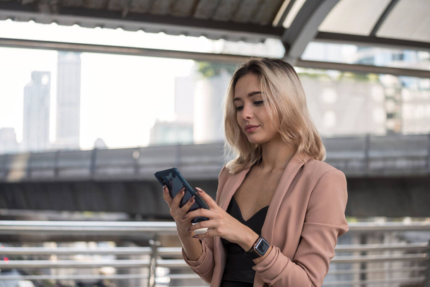 Smiling young beautiful American business woman in formal uniform check meeting schedule and chat by using corporate app on smart phone during transport in city. happy working woman with delight face. - Photo, Image