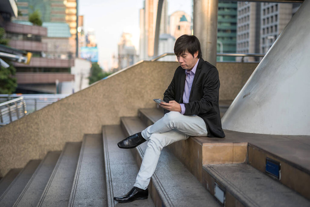 Geschäftige koreanische Geschäftsleute der 40er Jahre sitzen auf der Treppe und prüfen den Projektplan und den Terminplan in einer modernen Stadt. Arbeit am Handy während des Transports in der Stadt bei Sonnenuntergang. - Foto, Bild