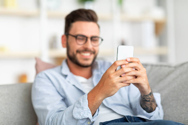 Feliz millennial chico disfrutando de chat de vídeo con el amante, mirando a la pantalla del teléfono inteligente y sonriendo, espacio libre - Foto, Imagen