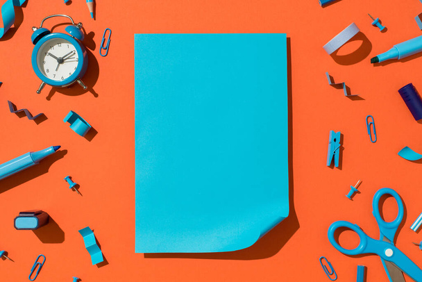 Вид зверху фото яскраво-блакитного аркуша паперу з закрученим кутом і шкільним приладдям сині канцелярські товари на ізольованому помаранчевому фоні з порожнім простором
 - Фото, зображення