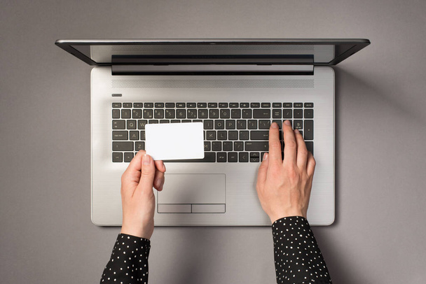 Primeira pessoa vista superior foto de mãos usando teclado laptop e segurando pequeno cartão branco retangular no fundo cinza isolado com espaço em branco - Foto, Imagem