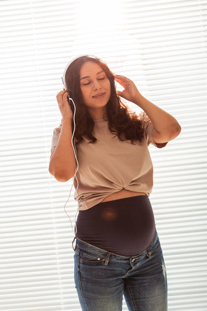 Pregnant woman listen to music in headphones at home and dances - Fotoğraf, Görsel