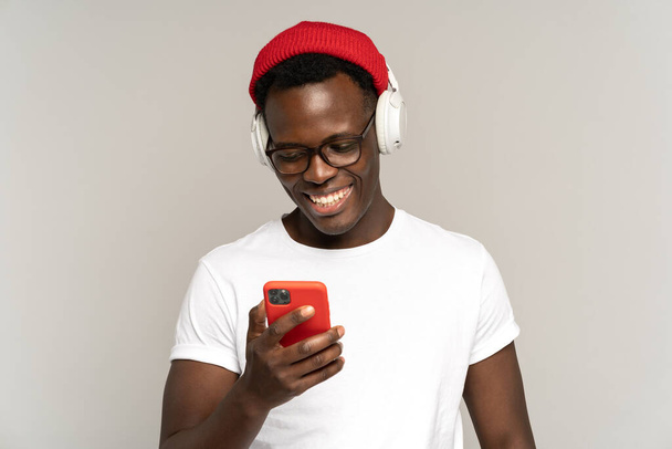 Homme noir écoute de la musique dans les écouteurs sans fil en utilisant les médias sociaux dans le smartphone. Plan studio.  - Photo, image