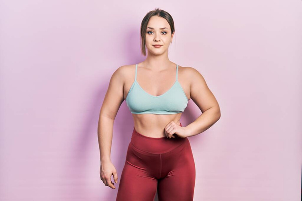 Jonge bodybuilder vrouw poseren tonen spieren staande dragen workout outfit - Foto, afbeelding