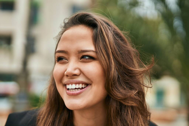 若いヒスパニック系の女性が幸せそうに街に立って笑っている. - 写真・画像
