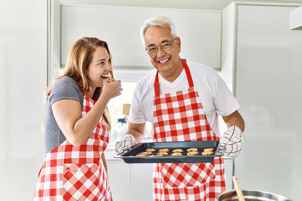 Middle age hispanic couple smiling happy baking cookies at the kitchen. - Photo, Image