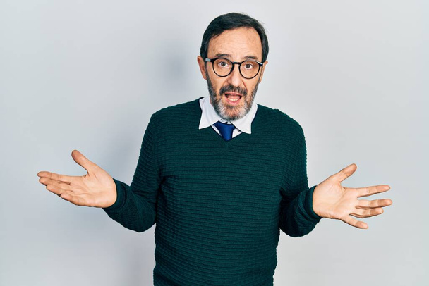 Middle age hispanic man wearing casual clothes and glasses clueless and confused expression with arms and hands raised. doubt concept.  - Photo, Image