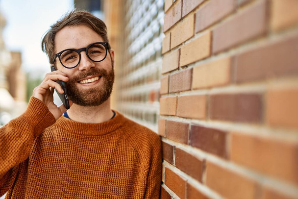 Белый мужчина с бородой разговаривает по телефону на улице в солнечный день - Фото, изображение