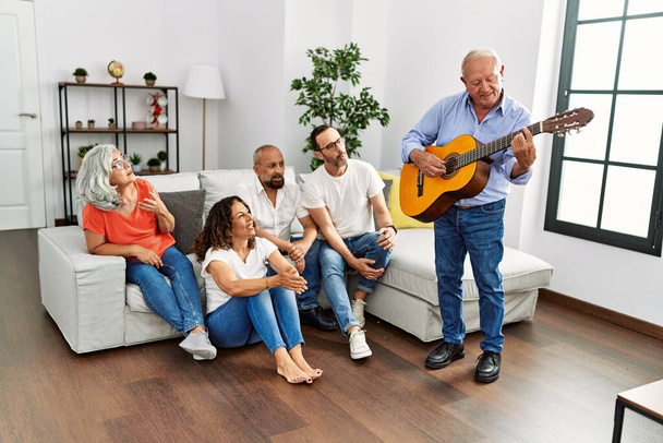 Groupe d'amis d'âge moyen faisant la fête en jouant de la guitare classique assis sur le canapé à la maison. - Photo, image