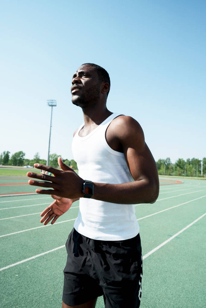 A black male track and field athlete in sports clothes is diligently preparing for a long distance at the stadium - Photo, image