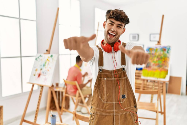 Mladý hispánec v uměleckém studiu schvaluje pozitivní gesto rukou, palce nahoru, usmívá se a je šťastný za úspěch. gesto vítěze.  - Fotografie, Obrázek