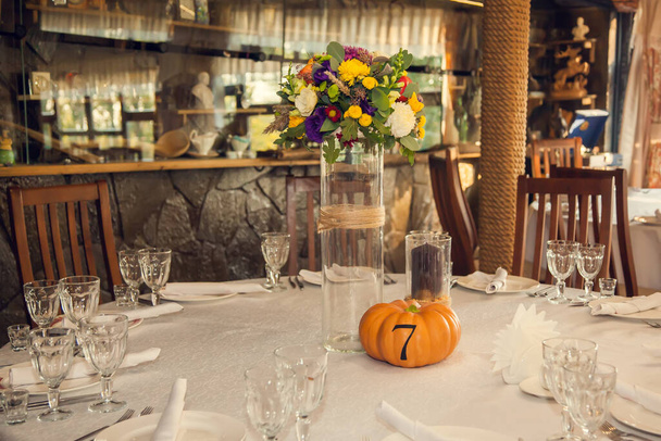 Feestelijke bloemisten in herfststijl met nummering van tafels op pompoenen in de feestzaal. Bloemisten en decoratie van evenementen bloemstukken. - Foto, afbeelding