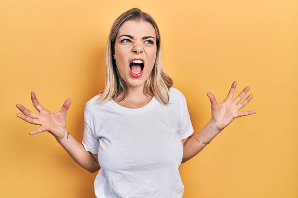 Beautiful caucasian woman wearing casual white t shirt crazy and mad shouting and yelling with aggressive expression and arms raised. frustration concept.  - Fotografie, Obrázek