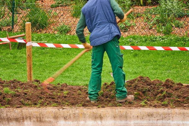 Trabajador utiliza azada para procesar la tierra en el parque de la ciudad
. - Foto, Imagen