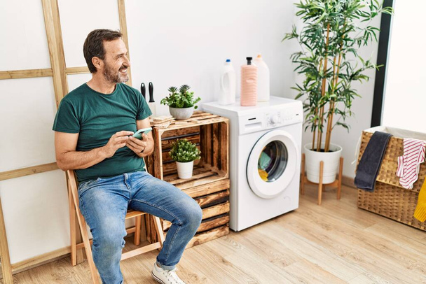Medioevo ispanico uomo dong lavanderia utilizzando smartphone in attesa a casa. - Foto, immagini