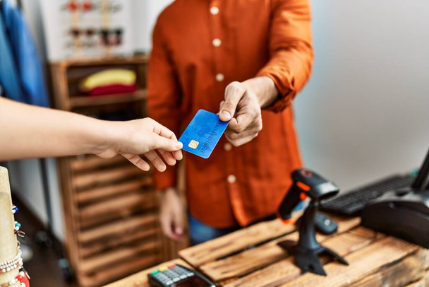 Ruka obchodníka, který dává kreditní kartu zákazníkovi v obchodě s oblečením. - Fotografie, Obrázek