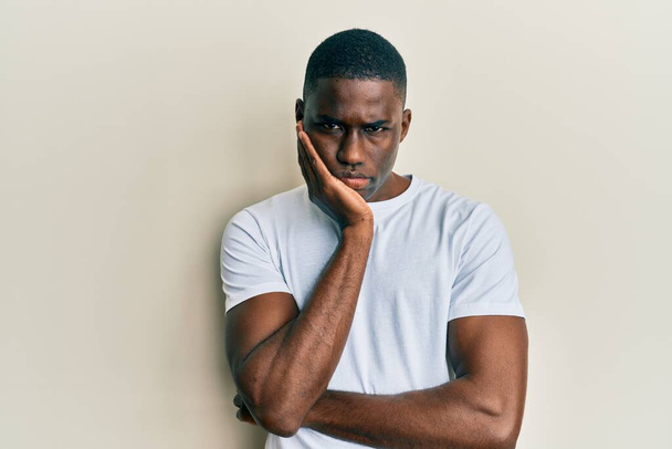 Jovem afro-americano vestindo casual t-shirt branca pensando que parece cansado e entediado com problemas de depressão com os braços cruzados.  - Foto, Imagem