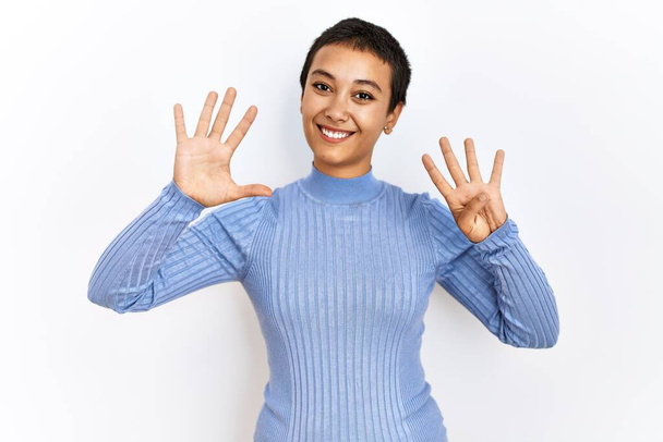 Fiatal spanyol nő, rövid hajjal, elszigetelt háttér felett áll, mutatva és mutatva a kilences számú ujjaival, miközben magabiztosan és boldogan mosolyog..  - Fotó, kép