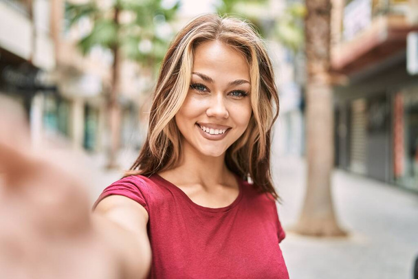 Jovem caucasiana sorrindo feliz fazendo selfie pela câmera na cidade. - Foto, Imagem