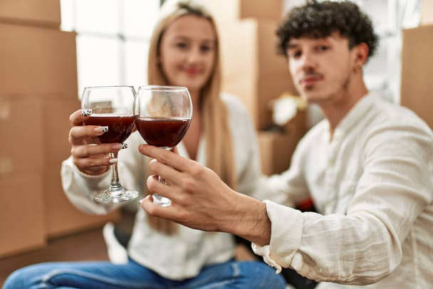 Jeune beau couple souriant heureux toasting avec du vin rouge à la nouvelle maison - Photo, image