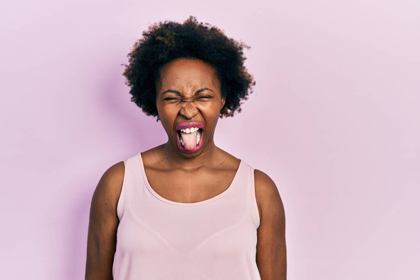 Mujer afroamericana joven que usa una camiseta casual sin mangas que saca la lengua feliz con expresión divertida. concepto de emoción.  - Foto, Imagen