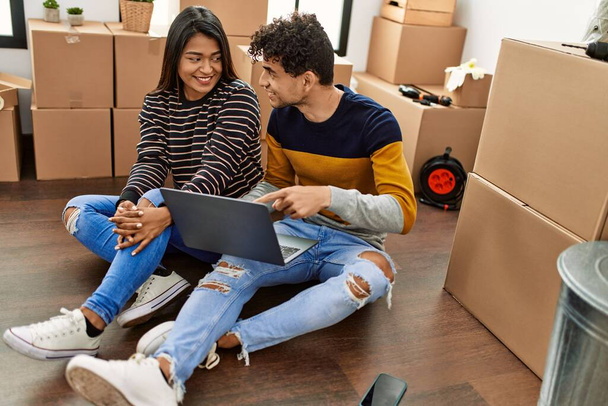 Jovem casal latino usando laptop sentado no chão em nova casa. - Foto, Imagem
