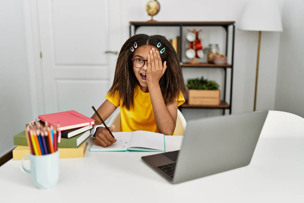 若いアフリカ系アメリカ人の女の子は家で宿題をしている手で片目を覆い、自信を持って笑顔と驚きの感情.  - 写真・画像